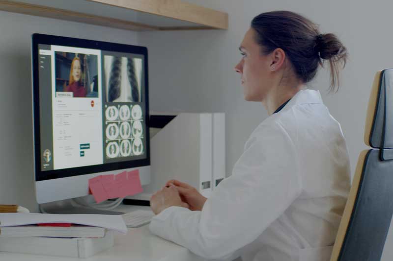 doctor conducting telehealth session with monitor showing patient and medical imaging