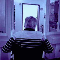 Elderly man in wheelchair indoor viewed from behind