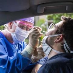 Man getting a nasal swab in his car by a medical specialist through a window.