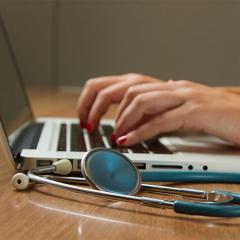 hands typing on a laptop with a stethoscope