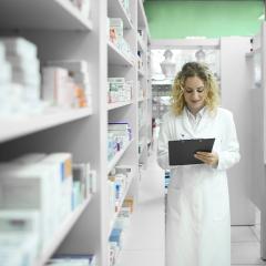 pharmacist writing on a notepad by a wall of pills. 
