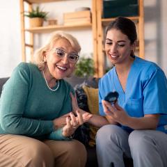 Nurse with elderly patient looking at glucose measuring device