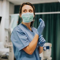 Female nurse with a mask putting on gloves 
